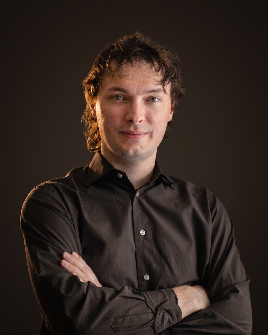 Jordan standing with his arms crossed in a dark studio, lit in warm light.